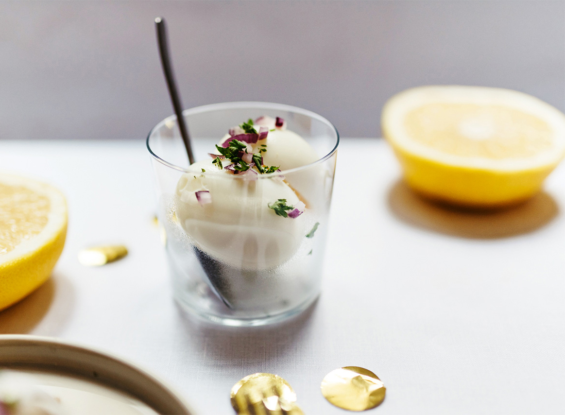 Glas mit gekochtem Ei, garniert mit roten Zwiebeln und Kräutern, mit einer Zitronenhälfte im Hintergrund.