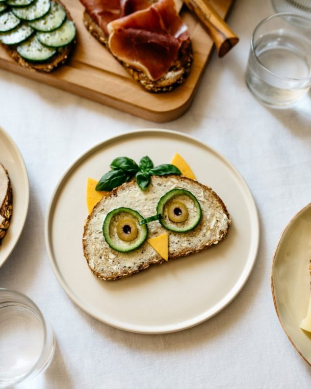 Wilde Eule Pausenbrot mit veganem Aufstrich Gurkenscheiben und Oliven als Augen Käseecken als Ohren und Basilikum als Federschmuck Kreatives Frühstücksbild aus der Corona-Zeit.