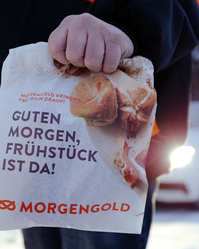 Hand hält Morgengold-Frühstückstüte mit Aufschrift ‚Guten Morgen, Frühstück ist da!