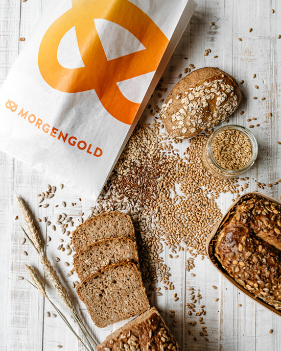 Vollkornbrot und Brötchen mit Körnern von Morgengold Frühstücksdienste, angerichtet mit Getreidekörnern auf Holzuntergrund.