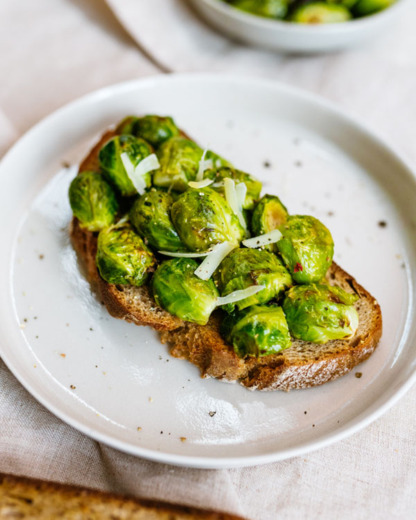 Gerösteter Rosenkohl auf einer Scheibe Vollkornbrot, serviert auf weißem Teller mit Pfeffer bestreut.