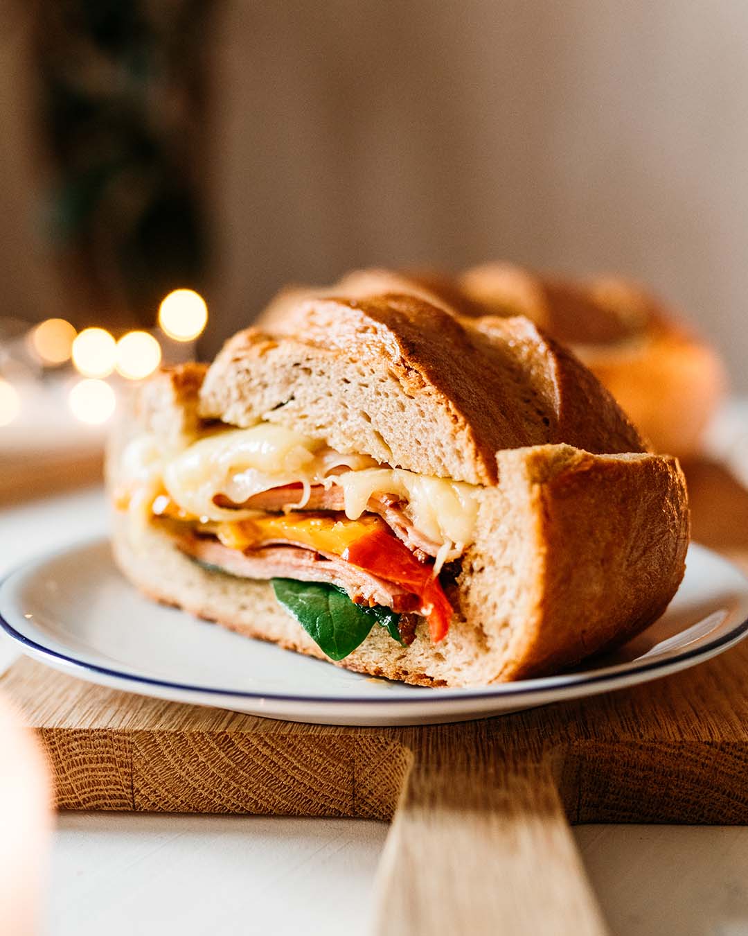 Nahaufnahme eines rustikalen Sandwiches mit geschmolzenem Käse, Schinken, Paprika und Spinat auf einem weißen Teller.