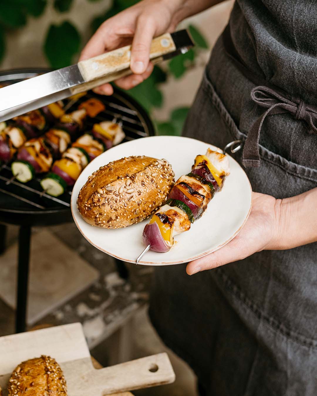 Gegrillter Schaschlik-Spieß mit buntem Gemüse und Sesambrötchen auf einem Teller – perfekt für sommerliches Grillvergnügen.