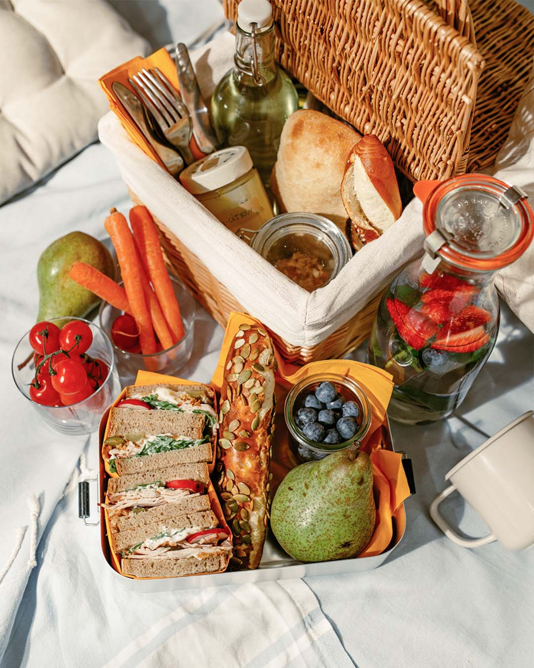 Sommerliches Picknick mit belegten Sandwiches, Karotten, Birne, Kürbiskernbrötchen, Beeren und aromatisiertem Wasser.