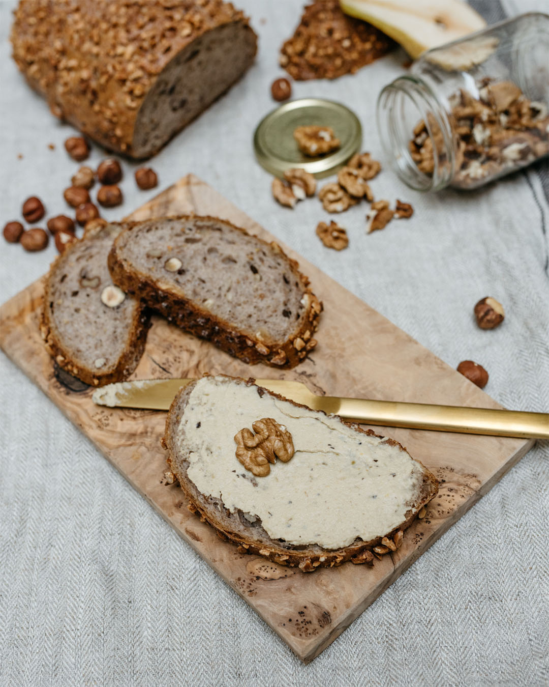 Nussbrot mit cremigem Walnussaufstrich, garniert mit einer Walnusshälfte auf Holzbrett mit goldener Messerklinge.