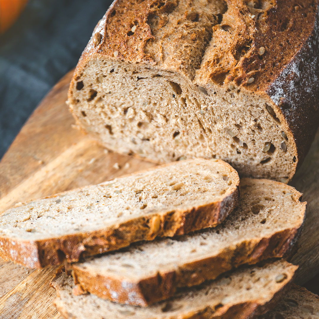 Frisch aufgeschnittenes Vollkornbrot mit lockerer Krume und dunkler Kruste auf einem Holzbrett.