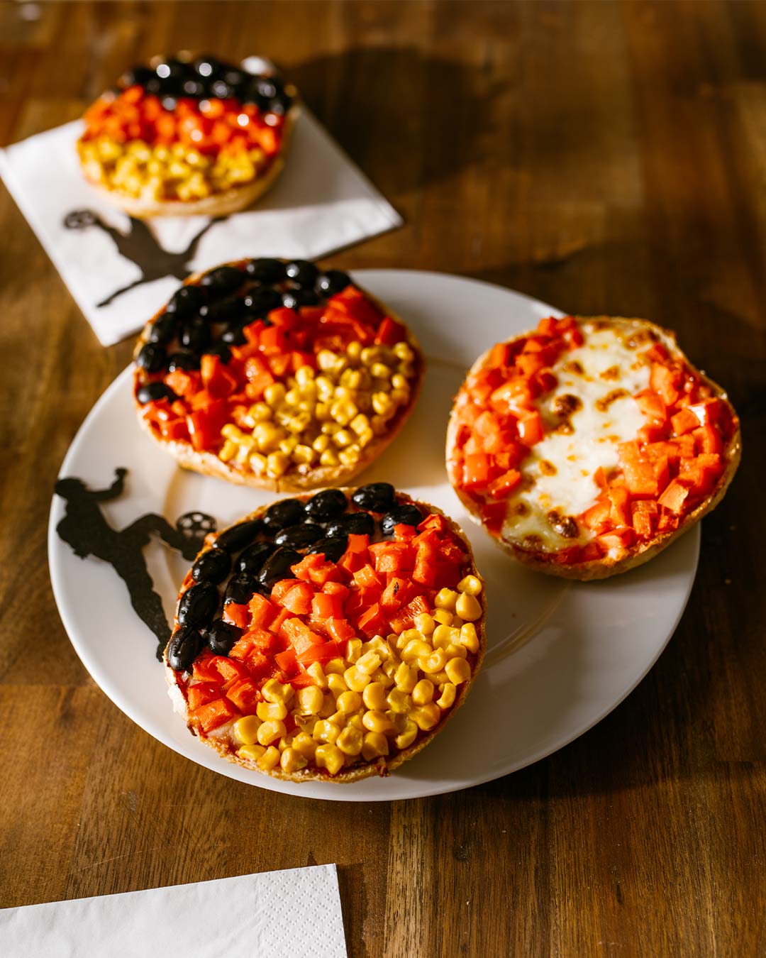 Pizzabrötchen in Deutschlandfarben mit Oliven, Paprika und Mais als kreative EM-Party Snacks auf einem Teller serviert.